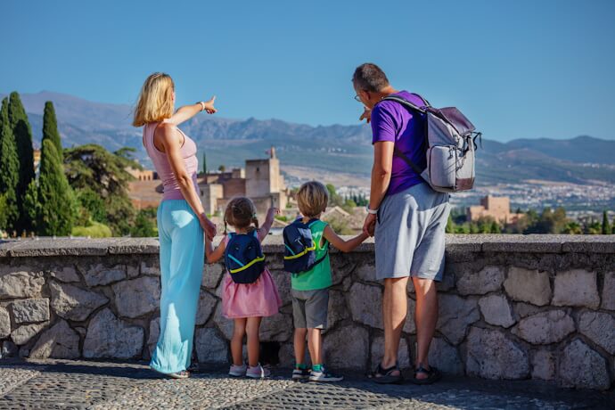 A family with two children enjoying a scenic view of the Alhambra in Granada with the Sierra Nevada mountains in the background.