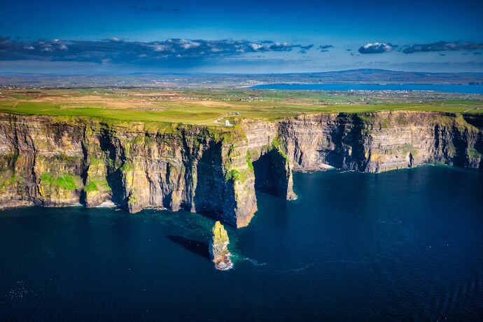 Aerial view of the dramatic Cliffs of Moher in County Clare, Ireland, rising above the deep blue Atlantic Ocean on a clear sunny day.