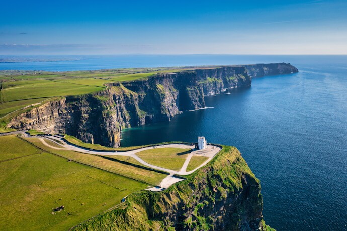 A dramatic aerial view of the towering Cliffs of Moher meeting the Atlantic Ocean under a clear blue sky.