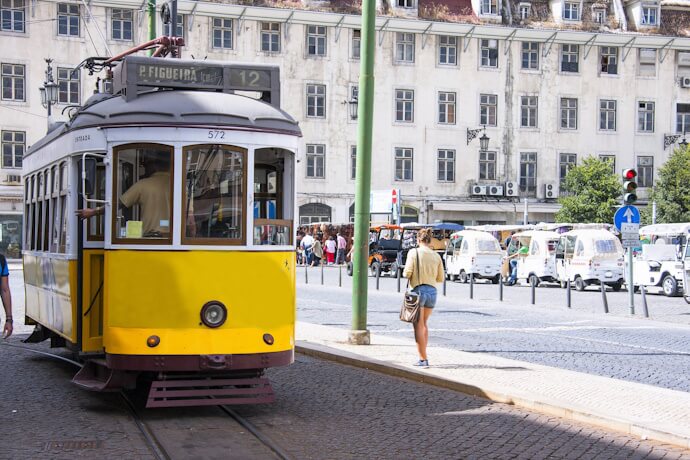 Classic yellow Lisbon tram stopped on a city street near Praça da Figueira with pedestrians nearby