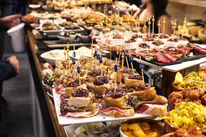 In San Sebastián’s Old Town, a spread of colorful pintxos lining the bar, with small bites topped with meats, seafood, and sauces.