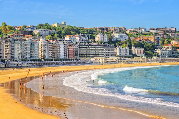 Along La Concha Beach in San Sebastián, a wide stretch of golden sand curves around the bay, with gentle waves and the city rising behind it.