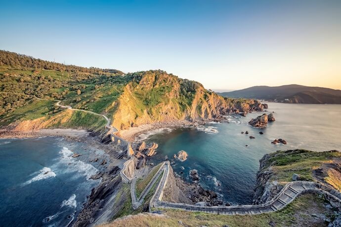 Along the Basque Coast, rugged cliffs meet the sea, with a winding path tracing the shoreline, offering wide views over the water.