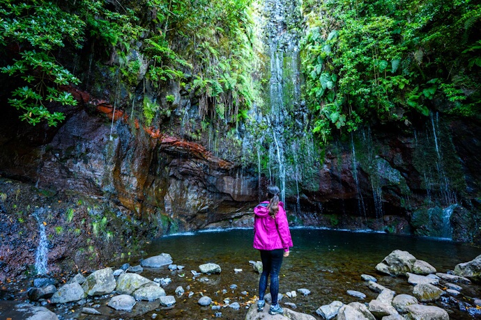 Woman standing by a lush Madeira waterfall in the Levada Trails