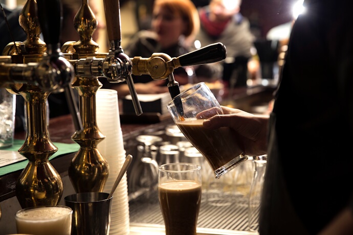 Bartender pouring a pint of Irish stout at a traditional pub bar.