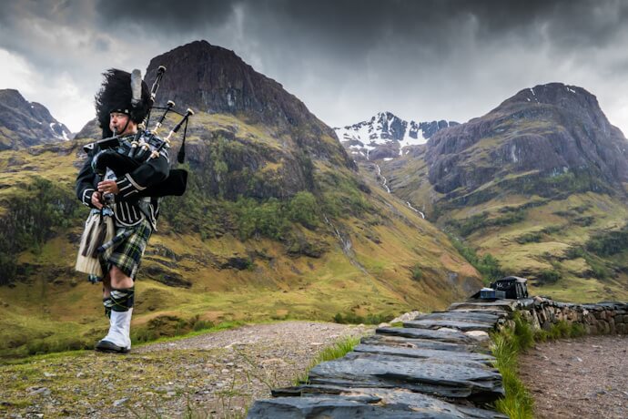 A bagpiper performing in the dramatic landscape of Glencoe.