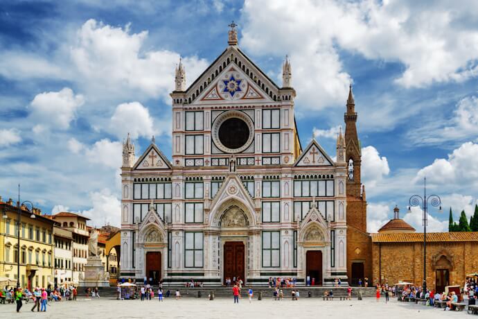 Façade of the Basilica of Santa Croce in Florence, Italy, with intricate Gothic architecture, colorful marble detailing, and a lively square filled with visitors.