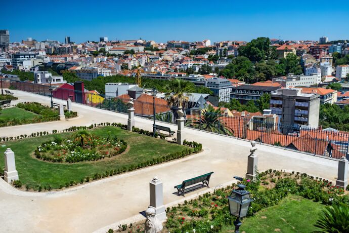 Landscaped viewpoint at São Pedro de Alcântara overlooking central Lisbon and São Jorge Castle on a sunny day.