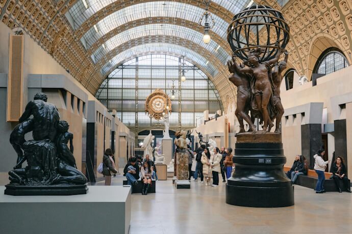 Interior of the Musée d’Orsay in Paris showcasing sculptures and a grand arched glass roof, with visitors exploring the art exhibits beneath a large ornamental clock.