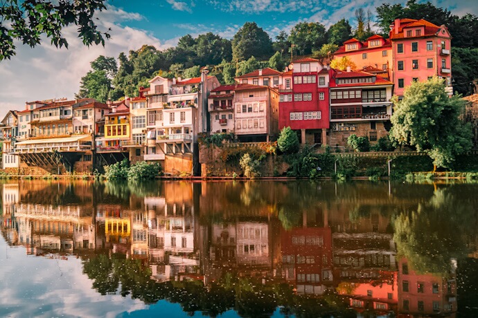 Vibrant houses perched along the riverbank in Amarante, Portugal, beautifully reflected in the calm waters with a backdrop of lush greenery.