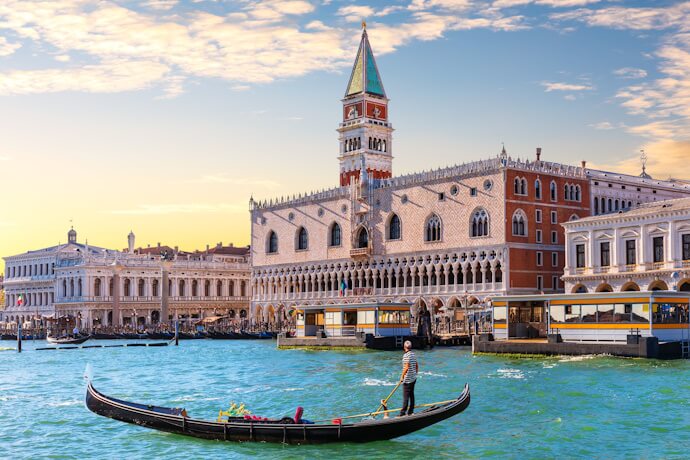Traditional gondola gliding along Venice’s Grand Canal at sunset, with the Doge’s Palace and St. Mark’s Campanile rising behind in the golden light.