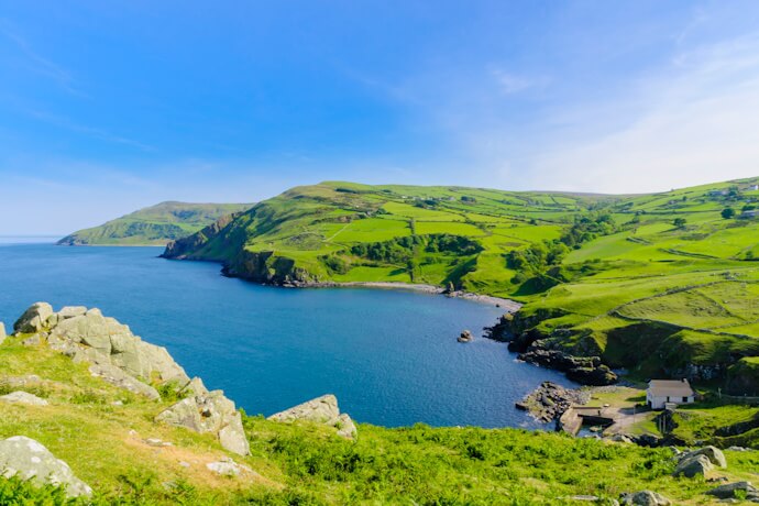 Lush green hills rolling down to a sheltered bay with turquoise waters.