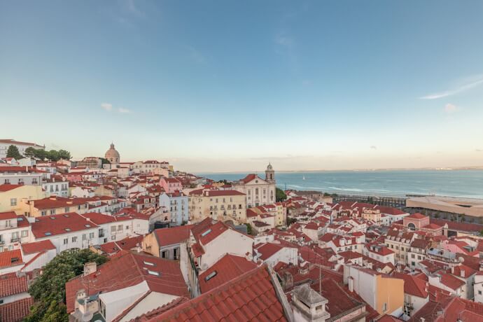 Elevated view from Portas do Sol across Lisbon's red rooftops toward the Tagus River and church domes.