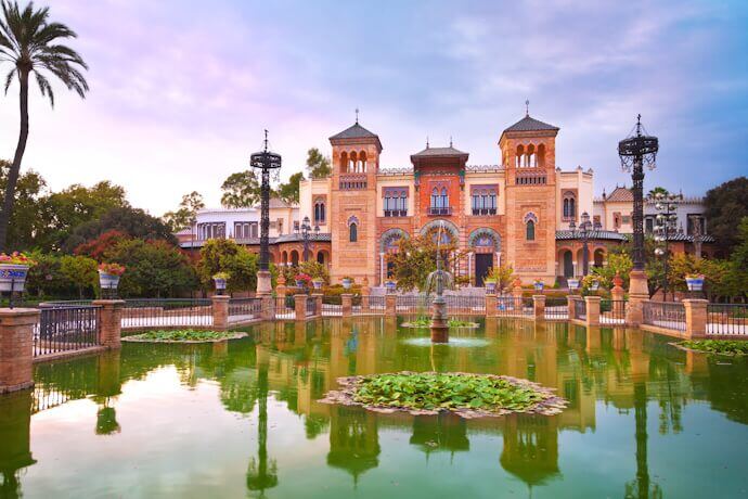 The stunning Royal Alcázar in Seville with Moorish and Renaissance influences against a soft, colorful sky.