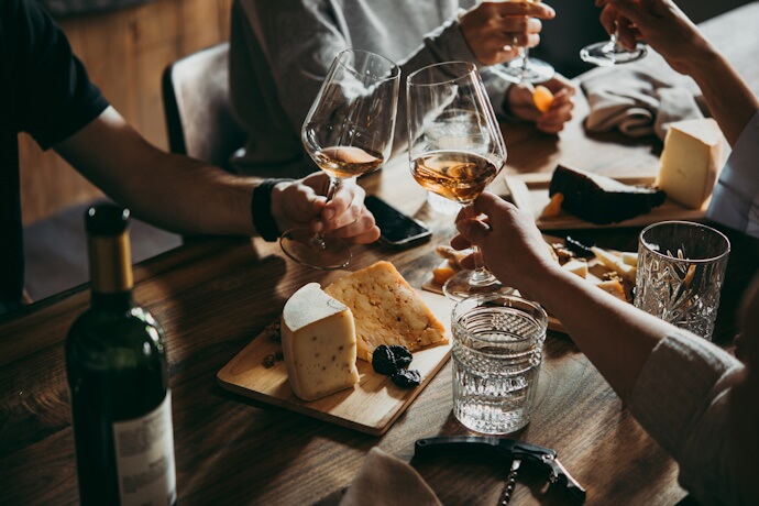 Friends gathered around a wooden table enjoying wine, cheese, and bread during a relaxed French meal.