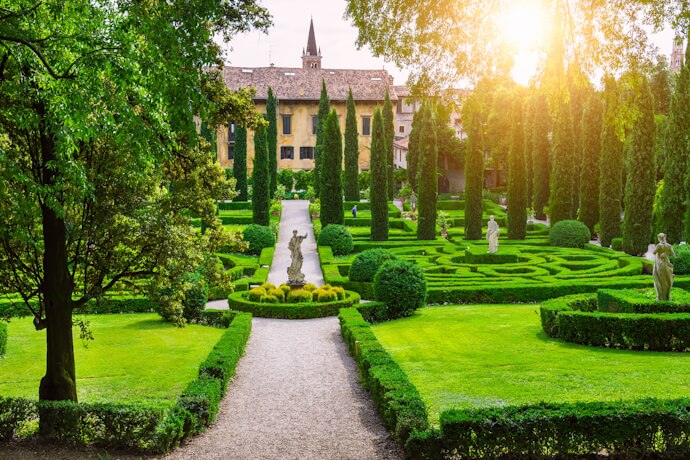 The beautifully manicured Renaissance gardens of Giardino Giusti in Verona, Veneto, Italy, featuring symmetrical green hedges, statues, and cypress-lined pathways, with a historic villa in the background bathed in warm sunlight.