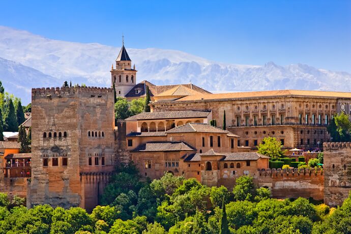 The Alhambra palace complex in Granada, surrounded by lush greenery with the Sierra Nevada mountains rising in the background.