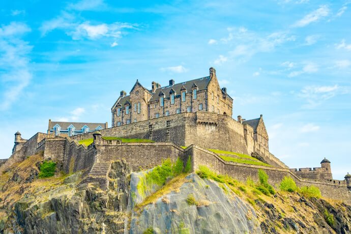 The imposing Edinburgh Castle perched dramatically atop Castle Rock, with sturdy stone walls and turrets against a clear, sunny sky.