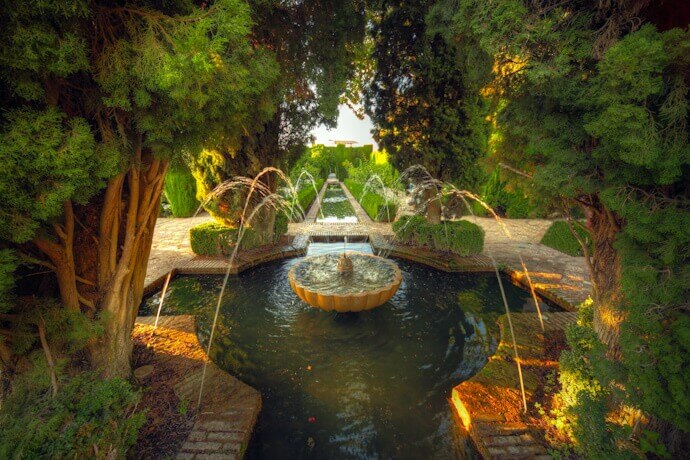 The tranquil Generalife gardens featuring a beautifully designed water fountain surrounded by lush greenery.