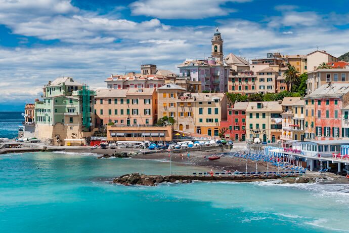 The charming seaside fishing village of Boccadasse in Genoa, Liguria, Italy, with colorful pastel houses clustered along a small pebbled beach and turquoise waters of the Ligurian Sea.