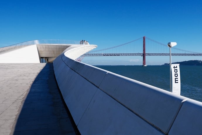 MAAT museum’s modern white terrace overlooking the Tagus River with the 25 de Abril Bridge in the background.