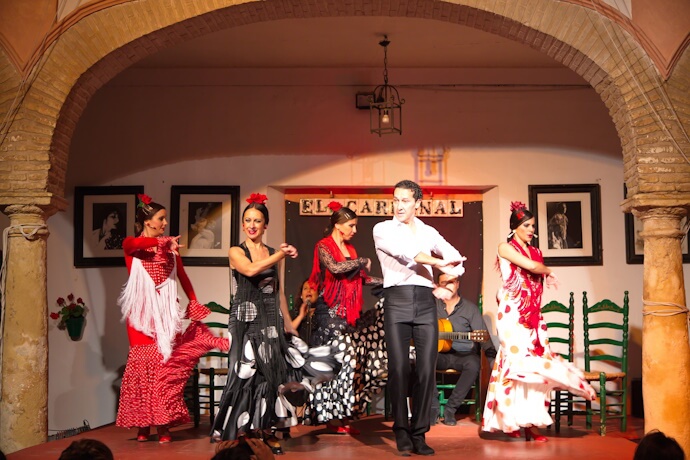 Flamenco dancers performing on stage in Seville, wearing traditional red, black, and white dresses.
