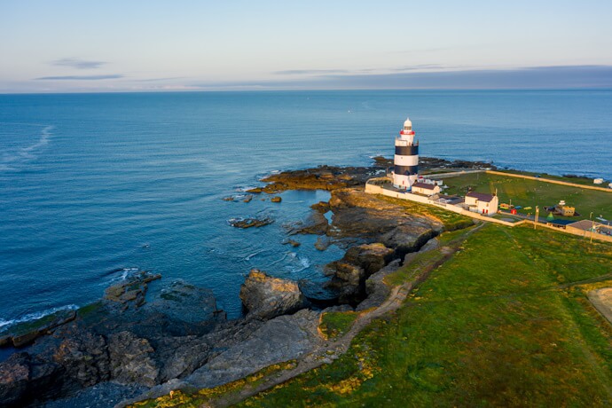 The black-and-white striped Hook Lighthouse standing on a rocky coastline at sunset.