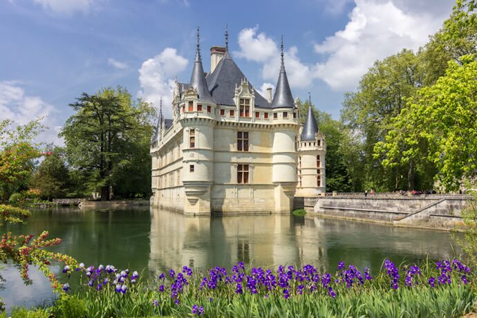 The elegant Château d’Azay-le-Rideau in France's Loire Valley, surrounded by a tranquil moat and blooming purple irises under a springtime sky.