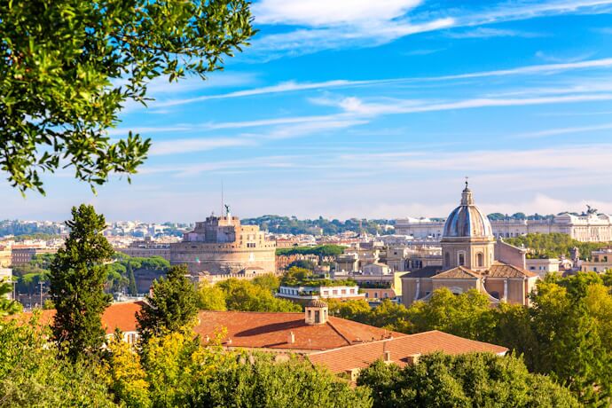 A panoramic view seen form the Gianicolo Terrace. In the midground, the cylindrical, formidable Castel Sant'Angelo stands prominently to the left, while a large domed church with a light-colored façade is visible to its right.