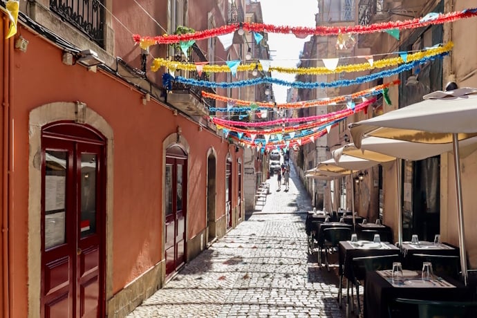 Colorful Lisbon street decorated with festive garlands and outdoor café tables along a cobblestone lane.