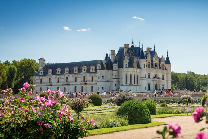 Elegant Château de Chenonceau in France framed by colorful flower gardens on a sunny summer day.