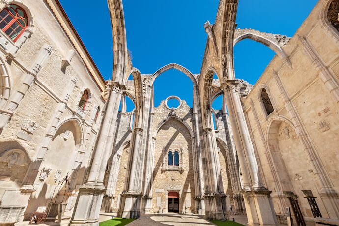 Gothic arches and open-air ruins of the Carmo Convent in Lisbon, set against a clear blue sky