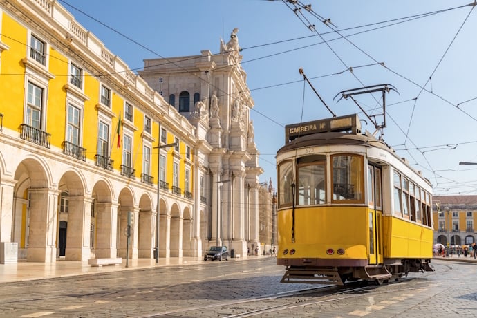 Iconic yellow Lisbon tram traveling through Praça do Comércio with grand yellow arcaded buildings.