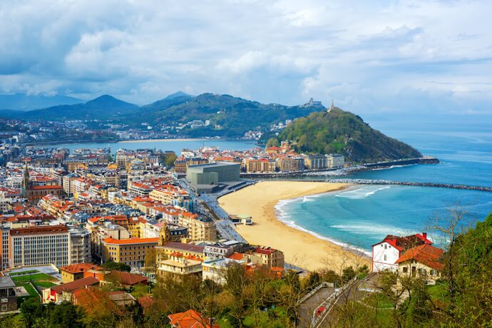 Aerial view of San Sebastián’s La Concha Bay with its sandy beach, coastal buildings, and green hills overlooking the shoreline.
