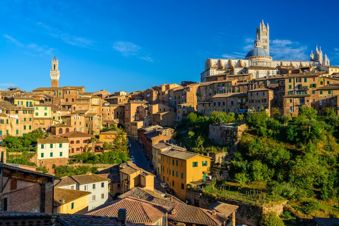 Historic hillside town of Siena with warm-toned buildings, winding streets, and the cathedral rising above the Tuscan landscape.