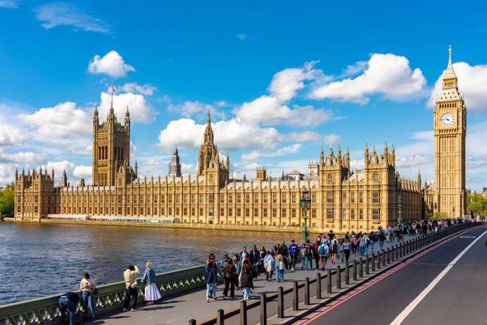 Tourists walking across Westminster Bridge with a full view of the Houses of Parliament and Big Ben on a sunny day.