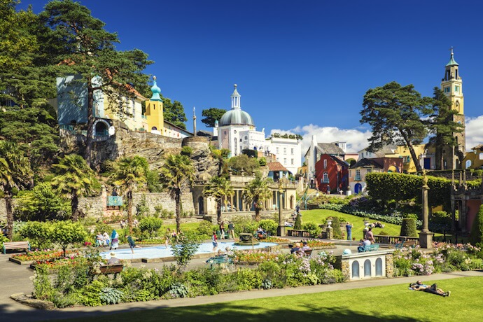 Colorful Italian-style village of Portmeirion in North Wales surrounded by lush gardens and visitors enjoying a sunny day.