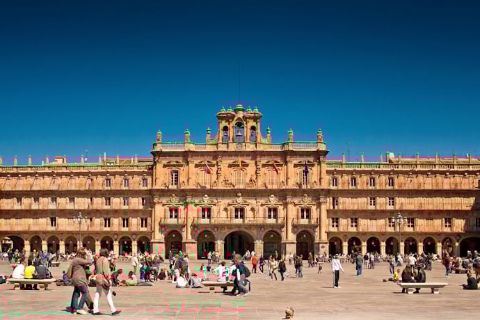 Lively Plaza Mayor of Salamanca, Spain, featuring Baroque architecture with uniform arcades and an ornate city hall façade, bustling with people relaxing and socializing.
