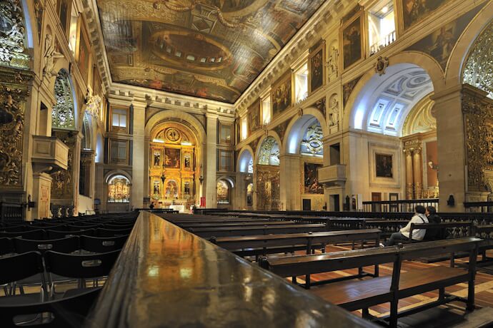 Interior of São Roque Church in Lisbon, featuring ornate gilded altars, painted ceilings, and wooden pews.