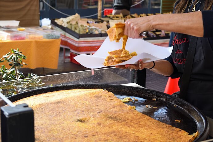 Vendor serving traditional socca at an outdoor market