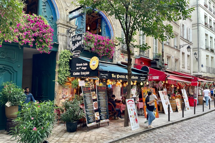 Charming pedestrian street in the Latin Quarter of Paris lined with colorful cafés and restaurants adorned with flower baskets and vibrant signage.