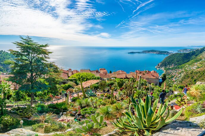 A panoramic view from Èze’s exotic garden, with cacti and succulents in the foreground, terracotta rooftops of the medieval village below, and the sparkling Mediterranean coastline stretching into the distance.