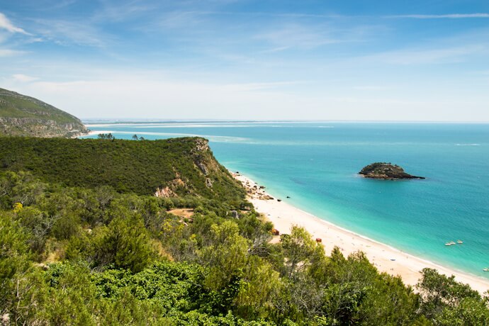 A serene beach with turquoise sea and green hills in Arrábida, Portugal.
