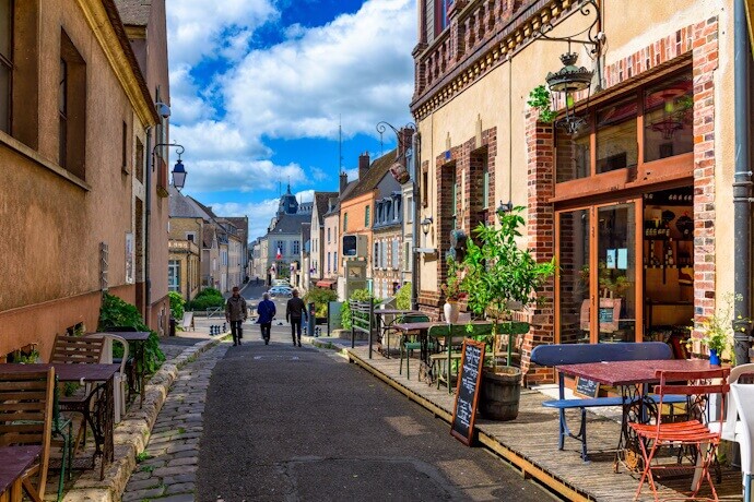 A charming cobblestone street in a French village, lined with colorful cafés and small shops