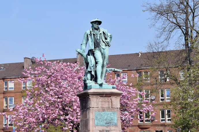 Statue of Scottish poet Robert Burns framed by blooming trees, set in a peaceful urban square.