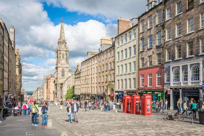 Edinburgh’s Royal Mile with historic stone buildings, red telephone boxes, and people walking along the cobbled street.