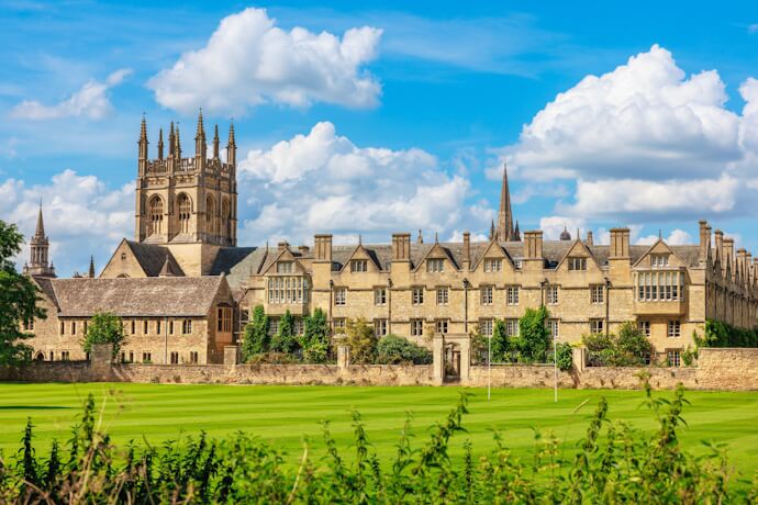 Historic buildings of the University of Oxford overlooking wide green lawns, showcasing classic stone architecture under a blue sky.