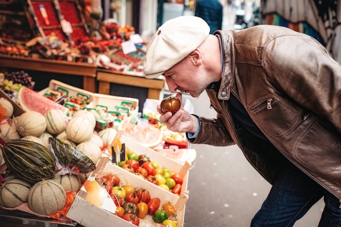 A shopper leaning in to smell fresh produce at a colorful stall.