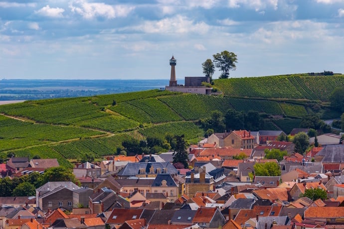 Rolling vineyard slopes lead to the Verzenay lighthouse above the village rooftops, with the Champagne plain stretching beyond.