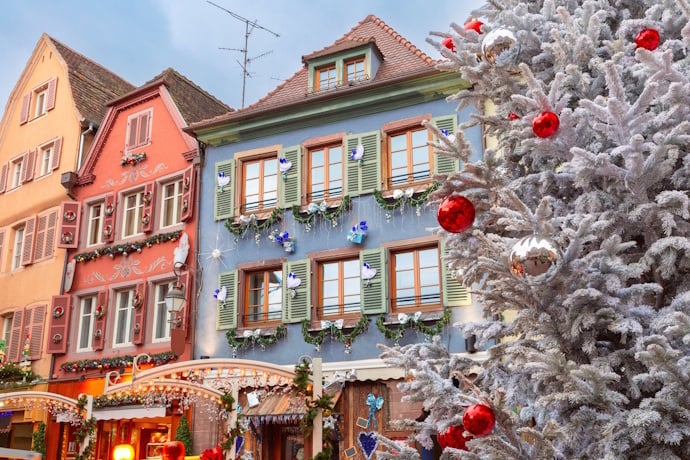 A festive street lined with pastel buildings, with a frosted Christmas tree sparkling in the foreground.